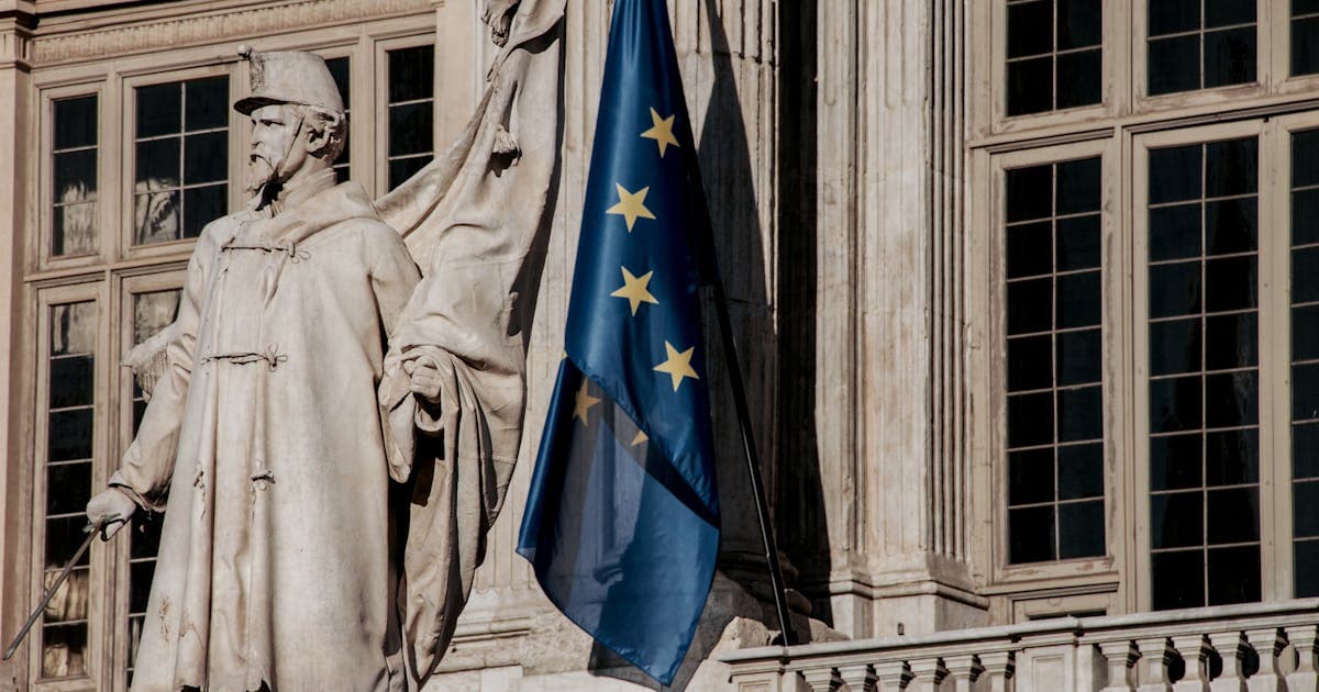 A statue beside the European Union flag, symbolising regulatory oversight of embedded finance