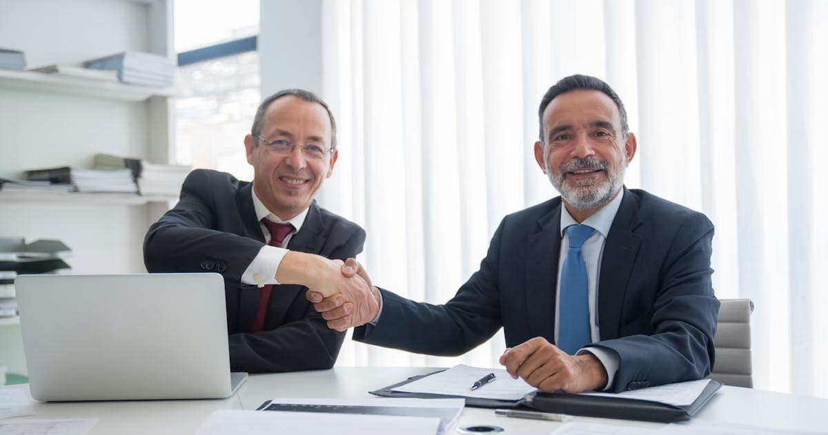 Two businessmen sealing a deal with a handshake, representing the reported Stripe-PayPal acquisition talks